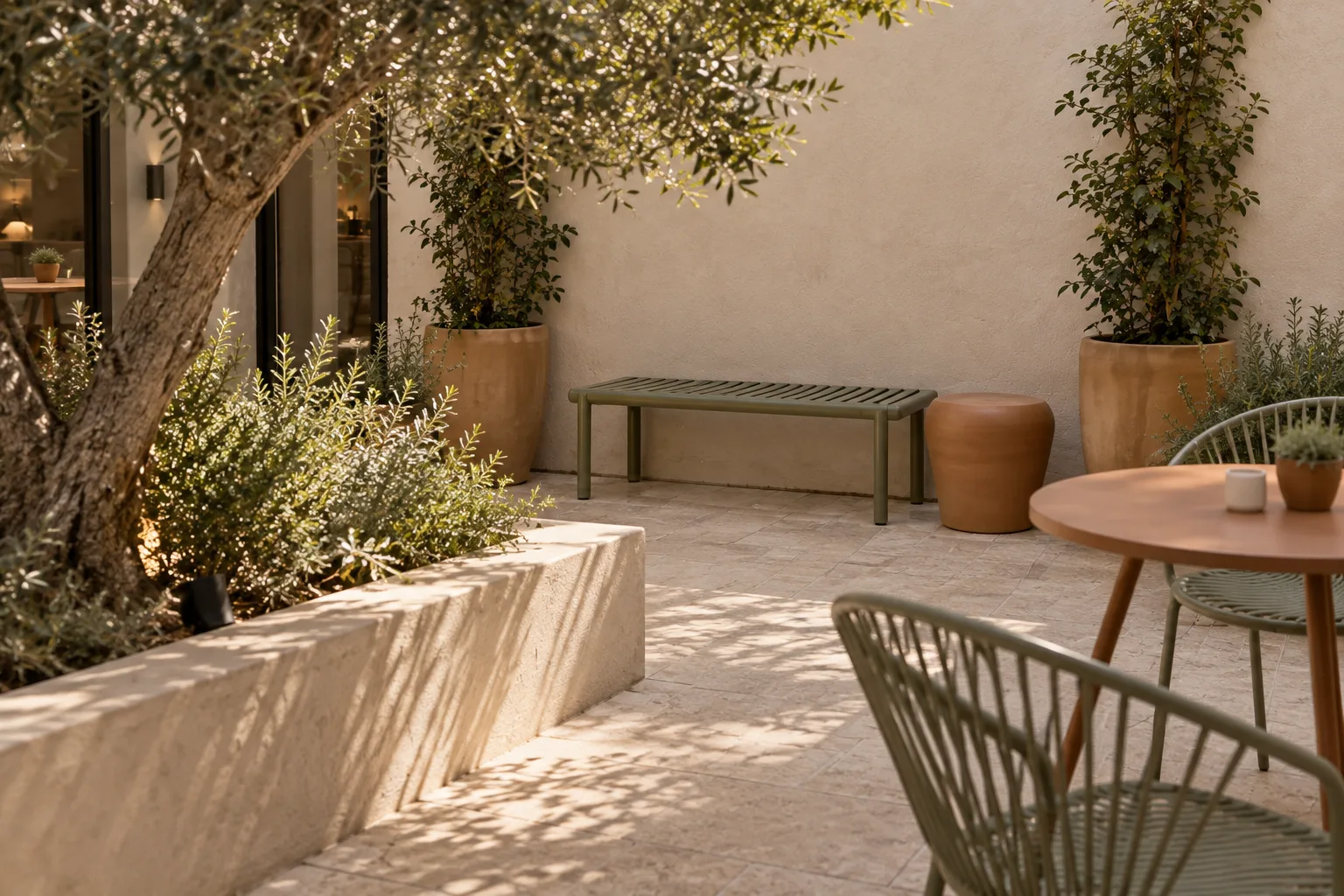 Backless sage slatted bench and low terracotta side table beside a modest courtyard planter
