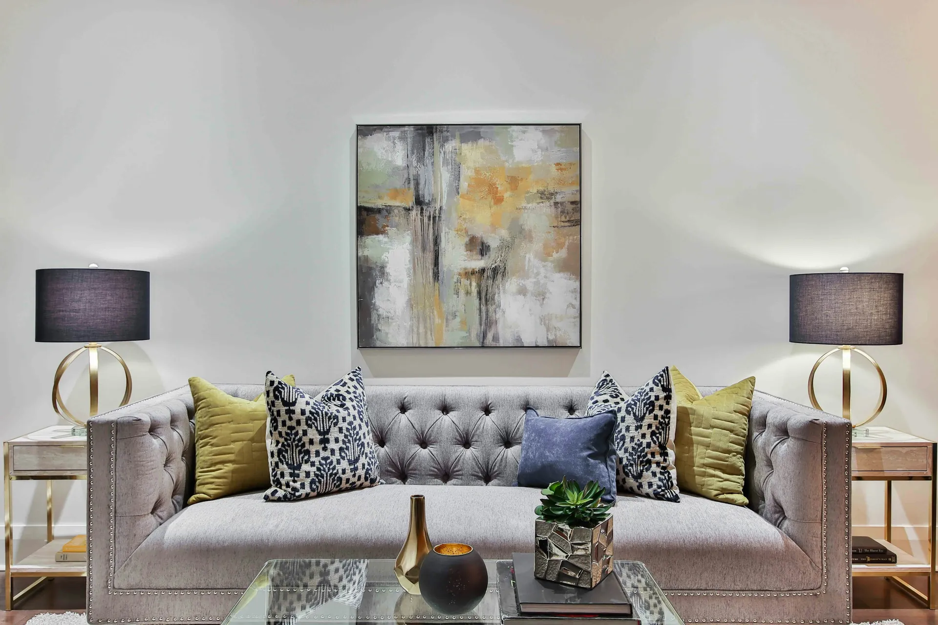 Tufted grey sofa with decorative cushions, table lamps, and abstract wall art