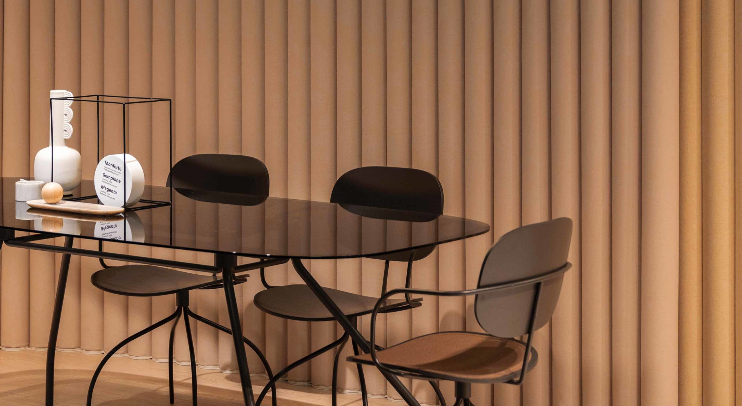 Dark glass dining table with black metal-frame chairs against a ribbed fabric wall